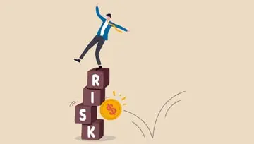 man balancing on blocks that spell out "risk" as a $ coin bounces by