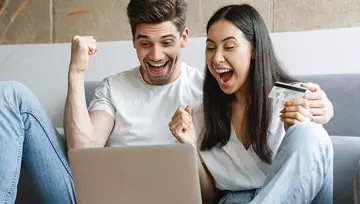 man and woman excitedly winning while playing on a laptop