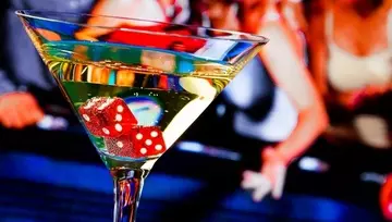 a cocktail with two red dice inside and casino goers in the background