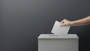 a woman's arm putting a voting envelope into a box.