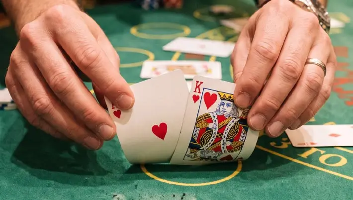 Person picking up the edges of 2 cards that show blackjack 