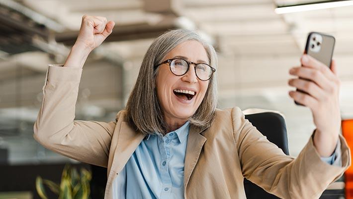 middle aged woman celebrating winning on her phone at Grande Vegas