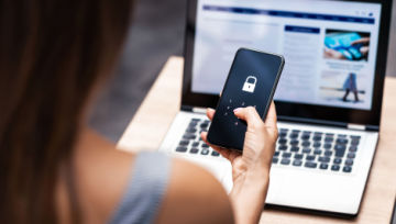 Woman holding a cell phone with an image of a lock while sitting near a laptop