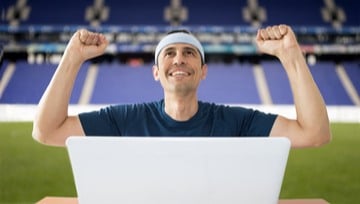 a guy dressed up for sport sitting in front of his laptop cheering on his team