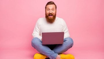 guy sitting playing on his laptop on a pink background