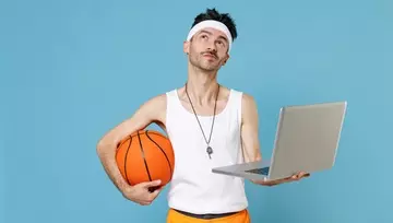 skinny guy wearing basketball clothes, holding a basketball and a laptop