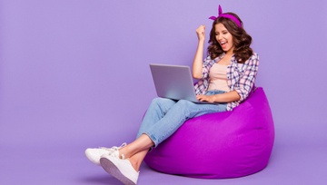 lady in a purple checked shirt and jeans playing on her laptop