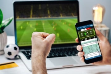 man celebrating a win on a sports event on his laptop and phone