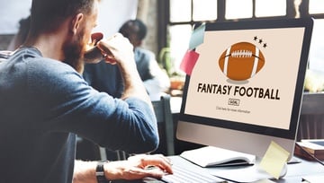 man sitting at his computer looking at fantasy football on his screen