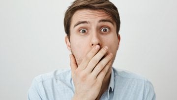 a man with his hand over his mouth in shock at hearing the scandalous news