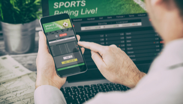 a man sports betting on his mobile and laptop