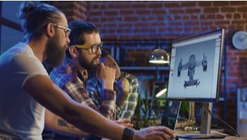 three men looking at a computer screen while designing a game