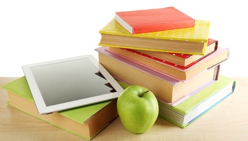 pile of books with an apple on top and a tablet leaning against it