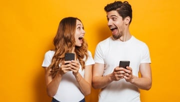 two friends playing online casino games on their phones on a yellow background