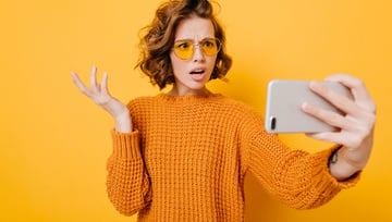 young woman in yellow sweater confused looking at her mobile phone on a yellow background