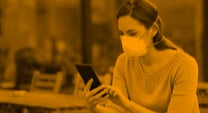 woman sitting at a coffee shop wearing a mask and looking at her phone