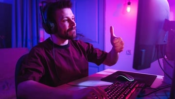 young man playing video games at home on his computer with a purple-ish background